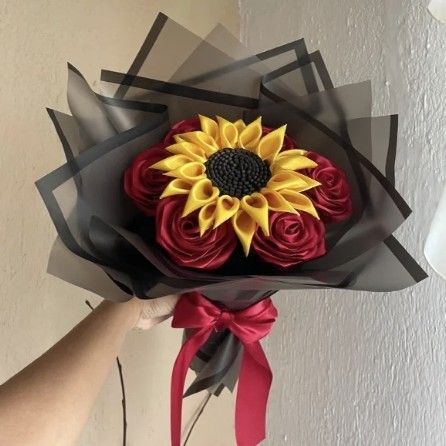 Ramo con un girasol al centro rodeado de rosas rojas, en papel negro con moño rojo
